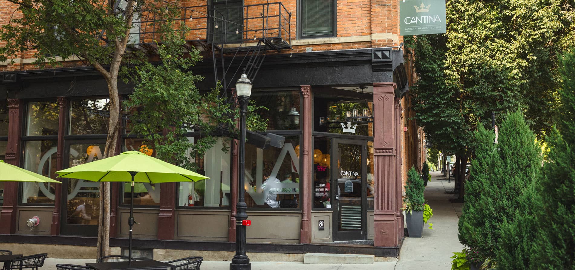 The Crown Cantina storefront on Broadway in Pendleton at dusk, with string lights and green patio umbrellas